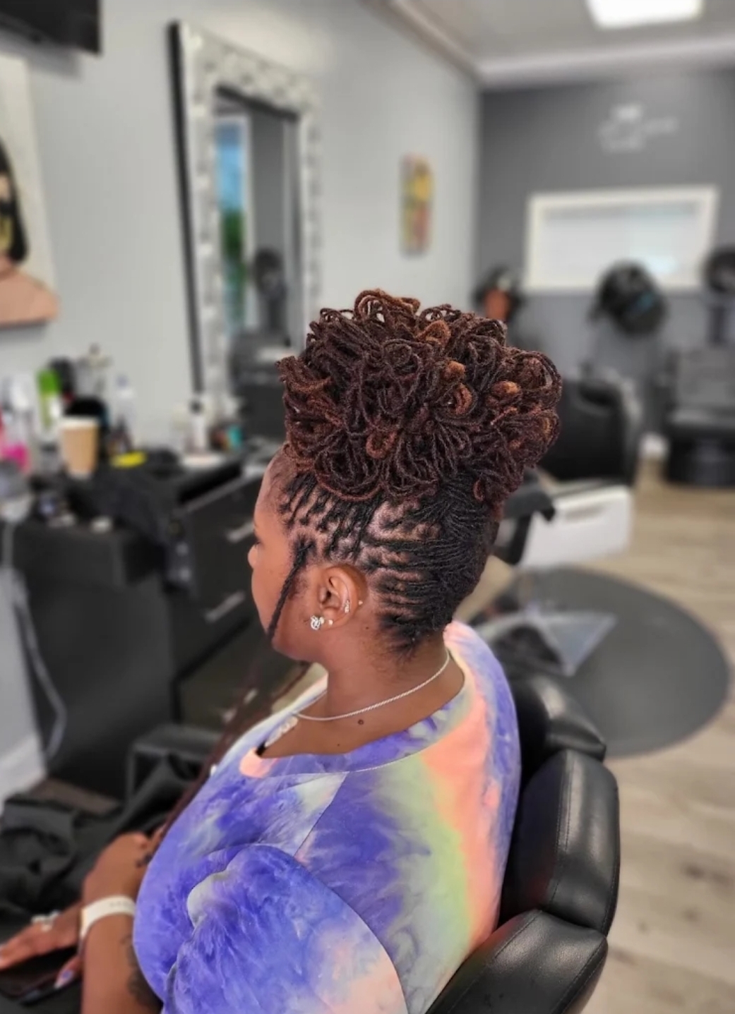 Loc updo woman in tie-dye top in salon chair — loc styling Delaware